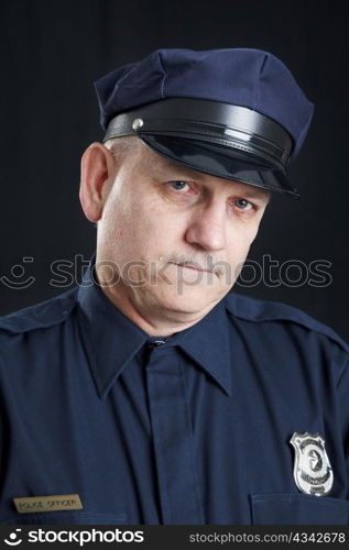 Sad police officer with a tear rolling down his face. Black background.