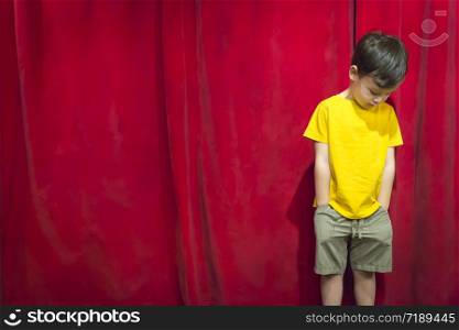 Sad Pouting Mixed Race Boy Standing In Front of Red Curtain.