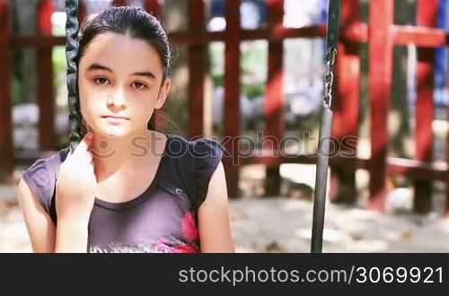 Sad preteen girl sitting on swing in playground