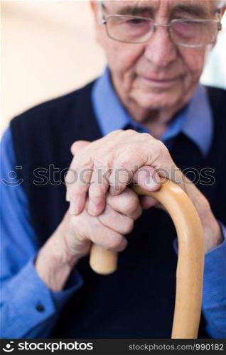 Sad Senior Man Sitting In Chair Holding Walking Cane
