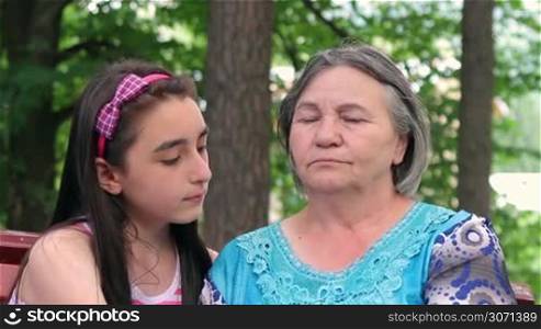 Sad senior woman hugged by her granddaughter - outdoor in the park.
