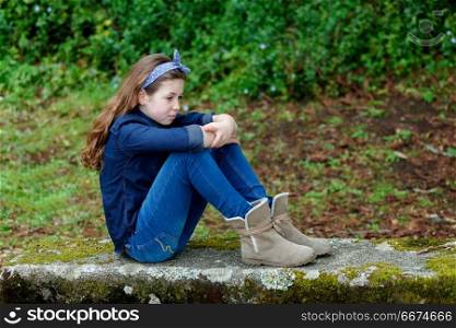 Sad small girl with ten years old sitting on a bench. Sad small girl with ten years old wearing a blue hair scarf sitting on a bench