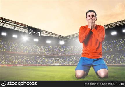 sad soccer player. unhappy soccer or football player kneeled down with hands on his face at stadium