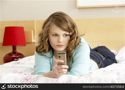 Sad Teenage Girl In Bedroom With Mobile Phone