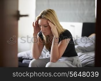 Sad Teenage Girl Sitting In Bedroom Whilst Boyfriend Sleeps
