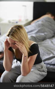 Sad Teenage Girl Sitting In Bedroom Whilst Boyfriend Sleeps