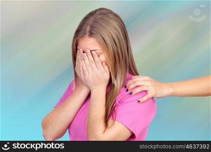 Sad teenager covering her face and a hand offering help isolated over a blue background