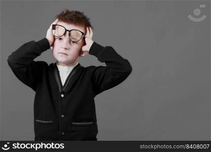 Sad unhappy schoolboy in eyewear having painful look, holding hand on his forehead. Frustrated sick child suffering form terrible headache.. Sad unhappy schoolboy in eyewear having painful look, holding hand on his forehead. Frustrated sick child suffering form terrible headache
