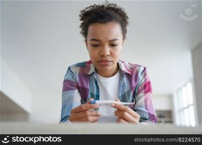 Sad unhealthy mixed race young girl holding electronic thermometer, has high body temperature, fever, covid symptom. Upset frowning teen lady caught cold durin coronavirus pandemic.. Upset unhealthy mixed race girl holding thermometer has high body temperature, fever, covid symptom