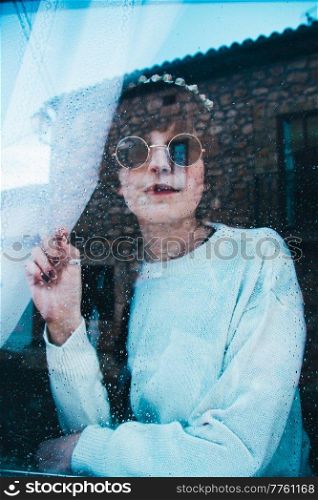 Sad woman alone in her home looking through a window in a rainy day