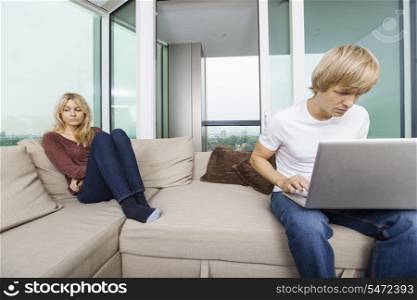 Sad woman beside man using laptop in living room at home