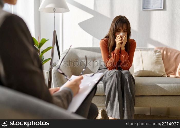 Sad woman crying crumpling napkins emotionally talking about problem to psychologist. Woman crying crumpling napkins talking to psychologist