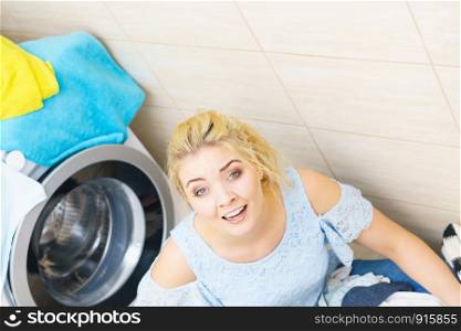 Sad woman having a lot of laundry to make. Unhappy female surrounded by big clothing piles stack sitting next to washing machine being tired houseworking.. Unhappy woman having a lot of laundry