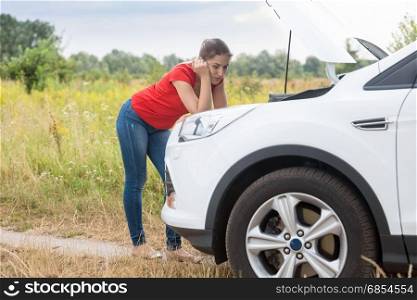 Sad woman looking on broken car at countryside