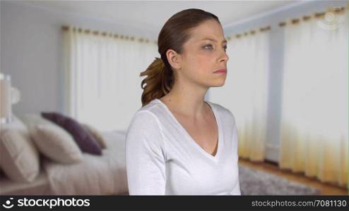 Sad woman looks into camera in a bedroom