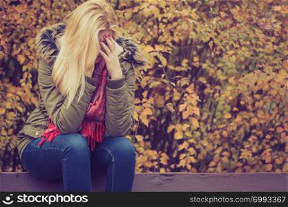 Sad woman sitting on bench in park during autumn weather hiding face in hand, feeling terrible depressed.. Sad woman sitting on bench in park hiding face