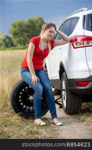 Sad woman sitting on tire and leaning on car at countryside road