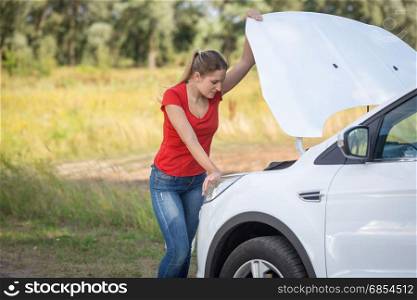 Sad woman standing at broken car on the roadside