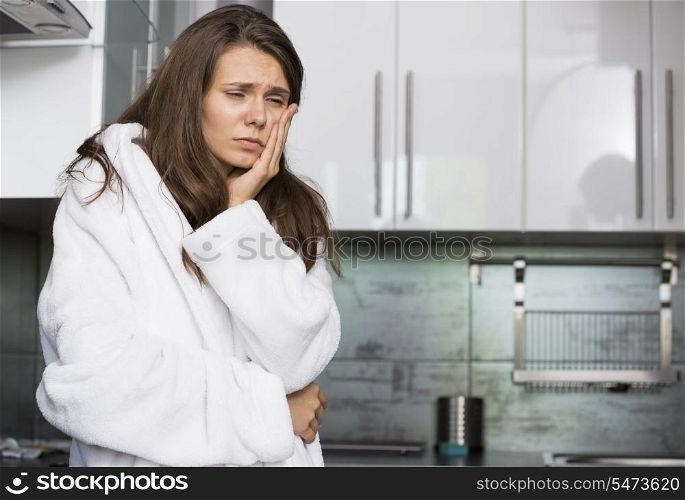 Sad woman suffering from toothache standing in kitchen