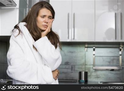 Sad woman suffering from toothache standing in kitchen