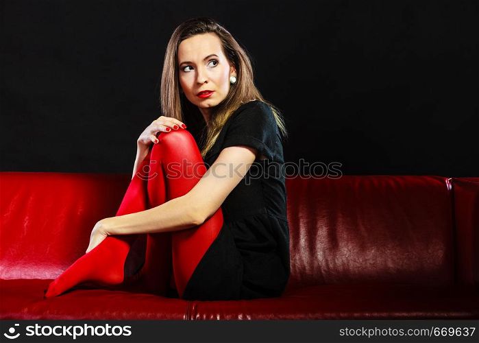 Sad woman vivid color pantyhose sitting on couch black background