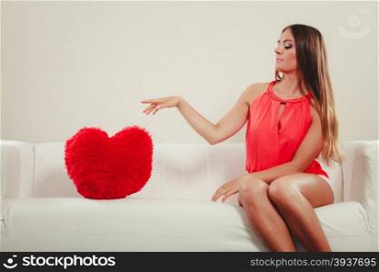 Sad woman with heart shape pillow. Valentines day.. Sad unhappy young woman girl with red heart shape pillow sitting on white sofa couch. Valentines day love.