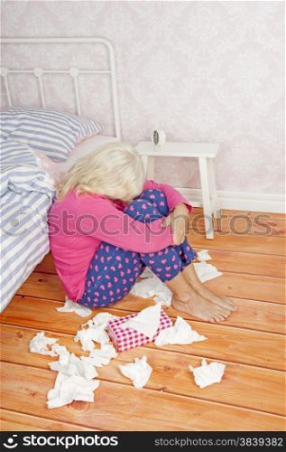 Sad woman with pink pajama and tissues sitting on floor against bed