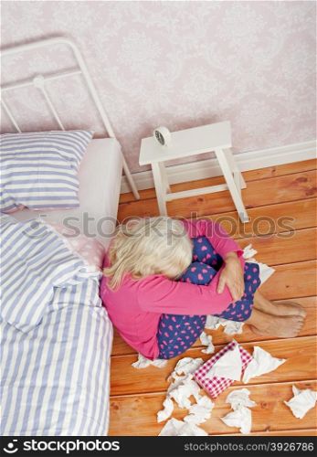 Sad woman with pink pajama and tissues sitting on floor next to bed