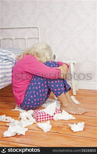 Sad woman with pink pajama and tissues sitting on floor next to bed