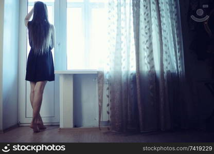 sad young adult woman sitting on a window