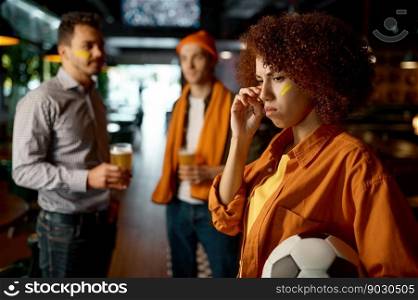 Sad young female football fan watching online match on tv screen in sports bar while rest with friends. Sad young female football fan watching match