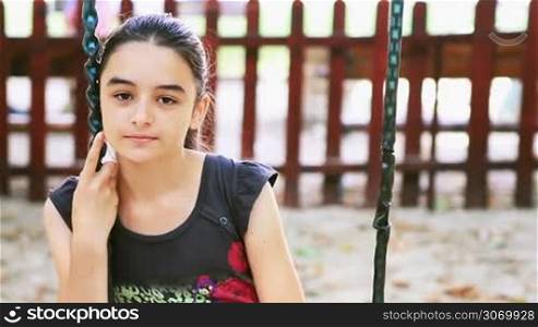 Sad young girl on swing in summer playground