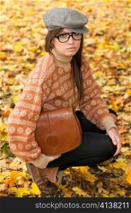 Sad young girl with handbag sitting on yellow autumn leaf background