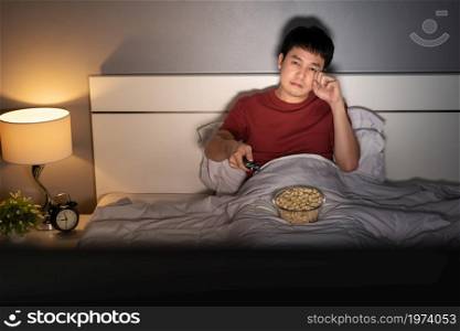 sad young man watching television and crying on a bed at night (romantic movie)