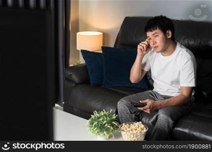 sad young man watching television and crying on sofa at night