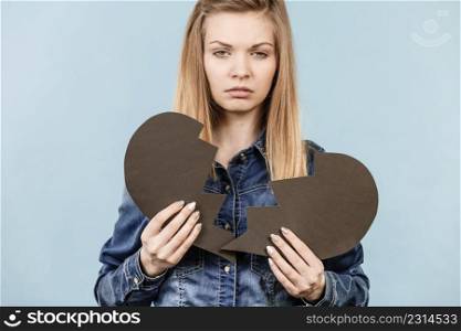 Sad young teenage woman with broken heart made of paper. Negative sad emotions, relationship problems concept. Shot on blue.. Young woman with broken heart