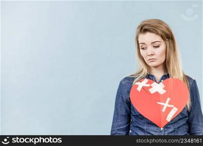 Sad young teenage woman with broken heart made of paper. Negative sad emotions, relationship problems concept. Shot on blue.. Young woman with broken heart