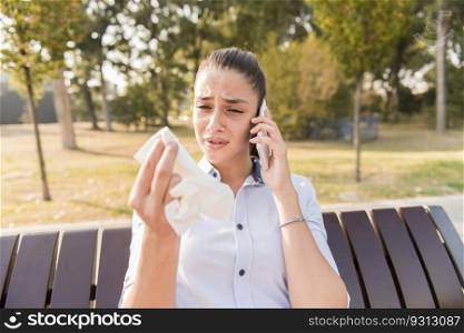 Sad young woman cries while talking on the mobile phone in the park on bench