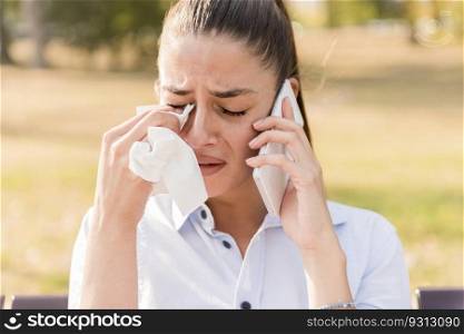 Sad young woman cries while talking on the mobile phone in the park on bench