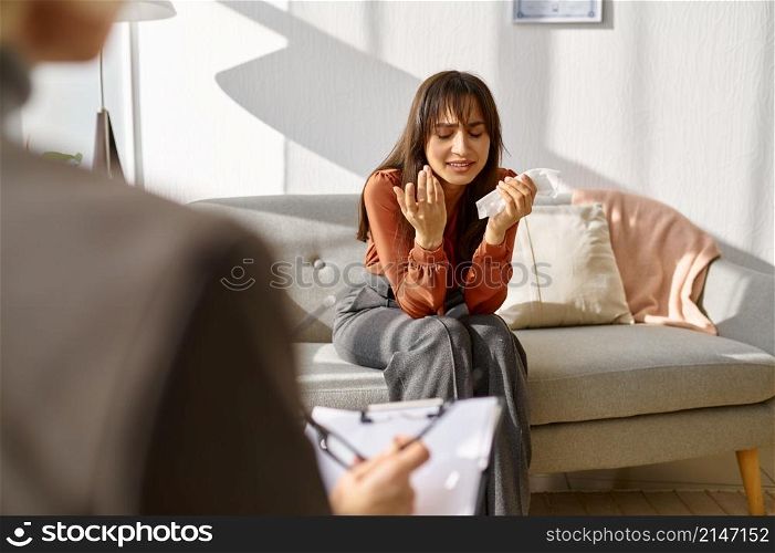Sad young woman crying crumpling napkins emotionally talking about problem to psychologist. Woman crying crumpling napkins talking to psychologist
