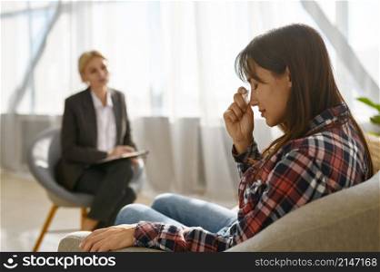 Sad young woman crying crumpling napkins emotionally talking about problem to psychologist. Woman crying crumpling napkins talking to psychologist