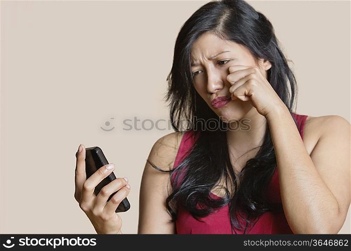 Sad young woman looking at mobile phone over colored background