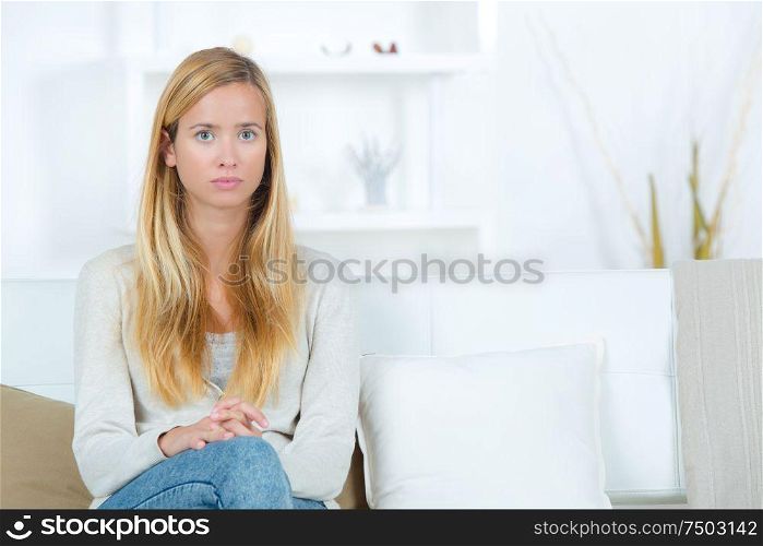 sad young woman sitting by sofa at home