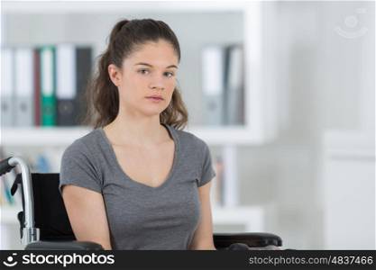 sad young woman sitting on wheelchair in room