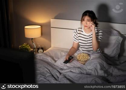 sad young woman watching television and crying on a bed at night (romantic movie)