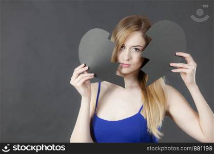 Sad young woman with black broken paper heart. Negative sad emotions, relationship problems concept, on dark.. Unhappy woman with broken heart.