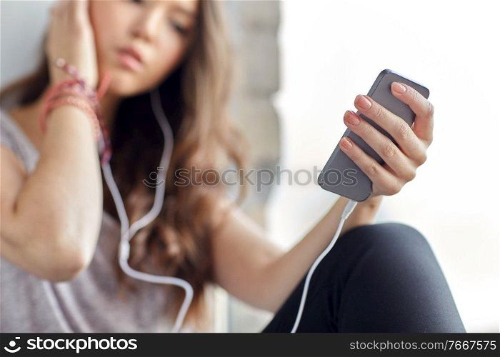 sadness and people concept - close up of teenage girl with smartphone and earphones listening to music at window. teenage girl with smartphone and earphones