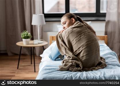 sadness and people concept - sad girl in blanket sitting on bed at home. sad girl in blanket sitting on bed at home