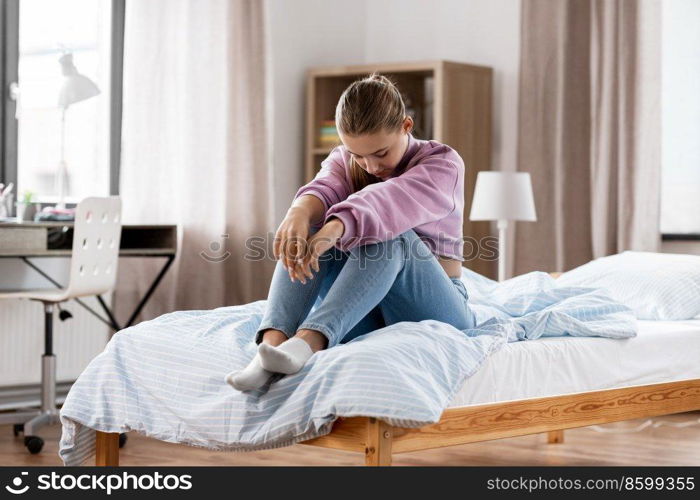 sadness and people concept - sad girl sitting on bed at home. sad girl sitting on bed at home