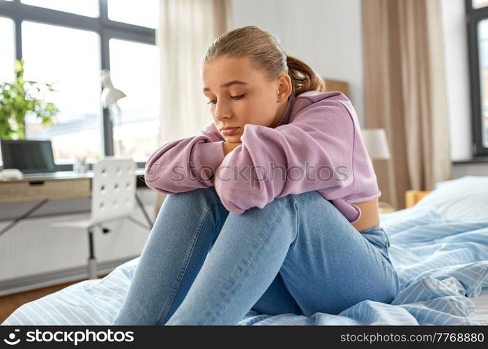 sadness, mental health and people concept - sad girl sitting on bed at home. sad girl sitting on bed at home